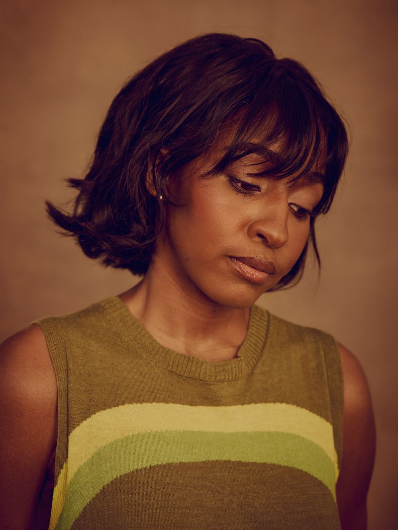 Portrait of Ayo Edebiri wearing a green striped sleeveless top against a warm textured background.