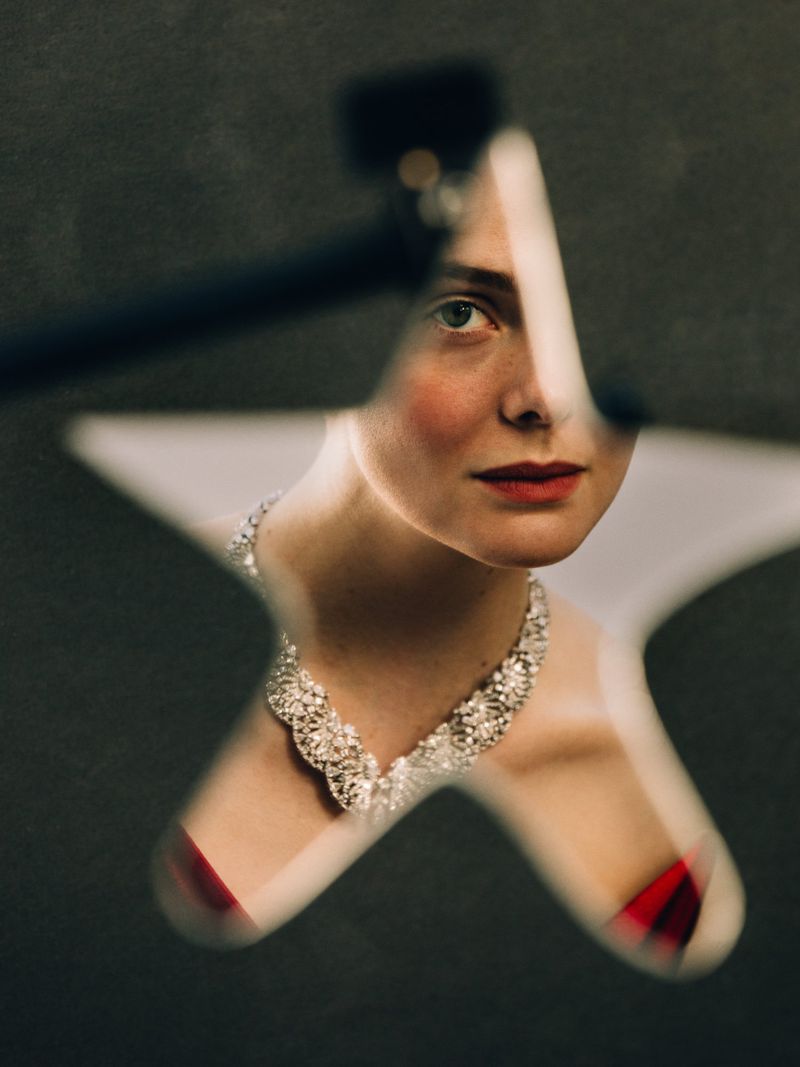 Elle Fanning wearing a diamond Cartier statement necklace seen through a star-shaped frame against a dark background.