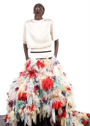 Model Awar Odhiang laughing in a cream top and voluminous multicolored feathered skirt against a pure white background.