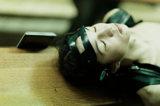 Model resting with eyes closed wearing a black cutout headpiece on a wooden surface backstage.