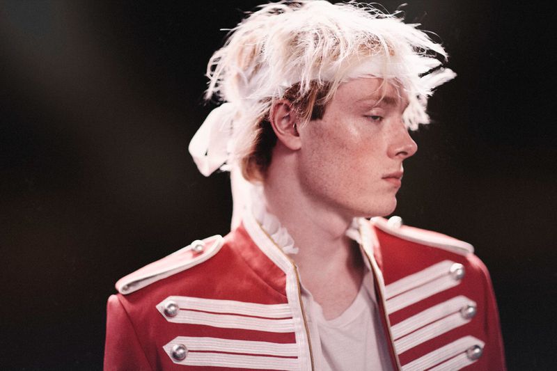 Model wearing a red military-style jacket with white detailing and messy white hair during Ann Demeulemeester SS26 Backstage