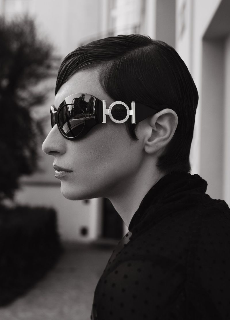 Profile shot of a stylish adult woman with short dark hair wearing oversized black sunglasses with a silver detail, outdoors.