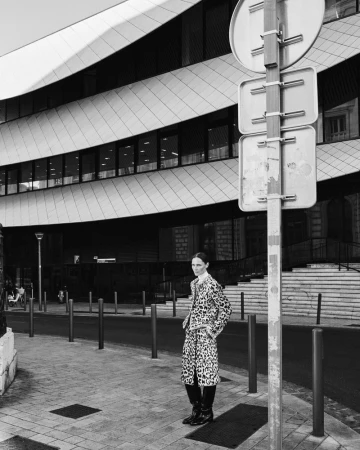 Model Tasha Tilberg standing on a city street wearing a leopard print patterned coat in front of modern architecture.