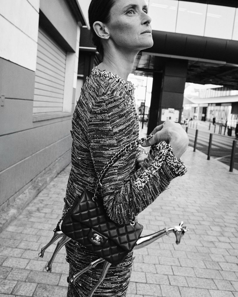 Tasha Tilberg standing outdoors wearing a textured tweed suit and carrying a black quilted crossbody bag and silver giraffe figurine.