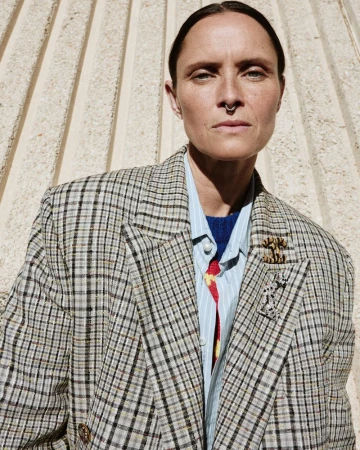 Tasha Tilberg wearing an oversized plaid blazer and striped shirt against a fluted concrete wall for Elle Canada.