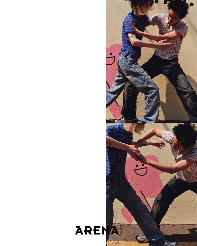 Two men face off on a city street by a painted wall, captured in a fashion editorial promoting youthful, urban style and camaraderie.