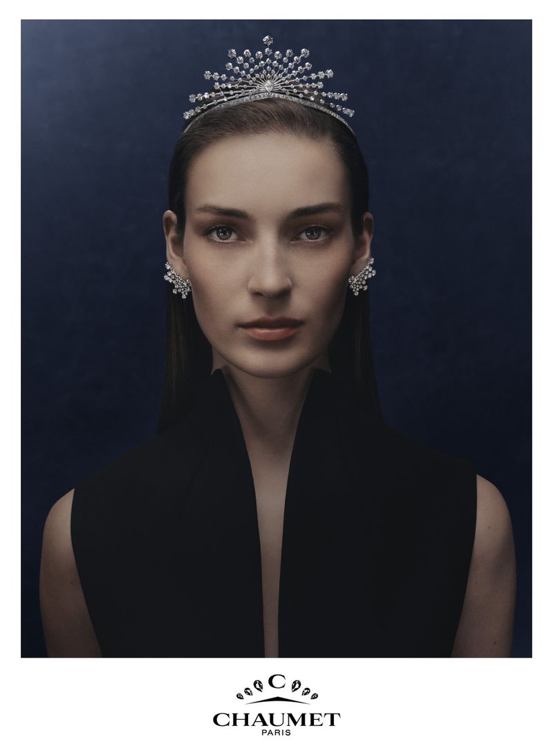 Model Julia Bergshoeff wearing an elaborate Chaumet diamond tiara and earrings with a black top against a dark blue background.