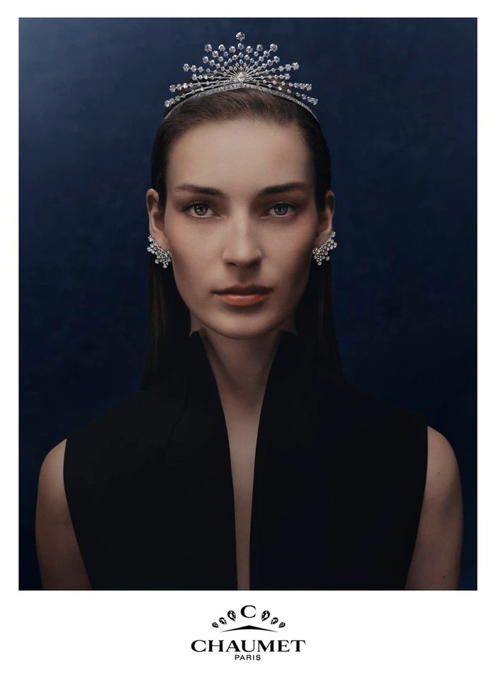 Model Julia Bergshoeff wearing an elaborate Chaumet diamond tiara and earrings with a black top against a dark blue background.
