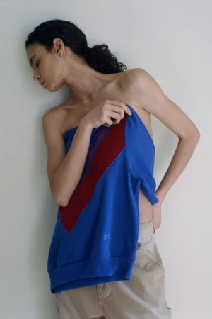 Model Luma Vitoria holding a draped blue and burgundy top against an off-white seamless backdrop for Wales Bonner.
