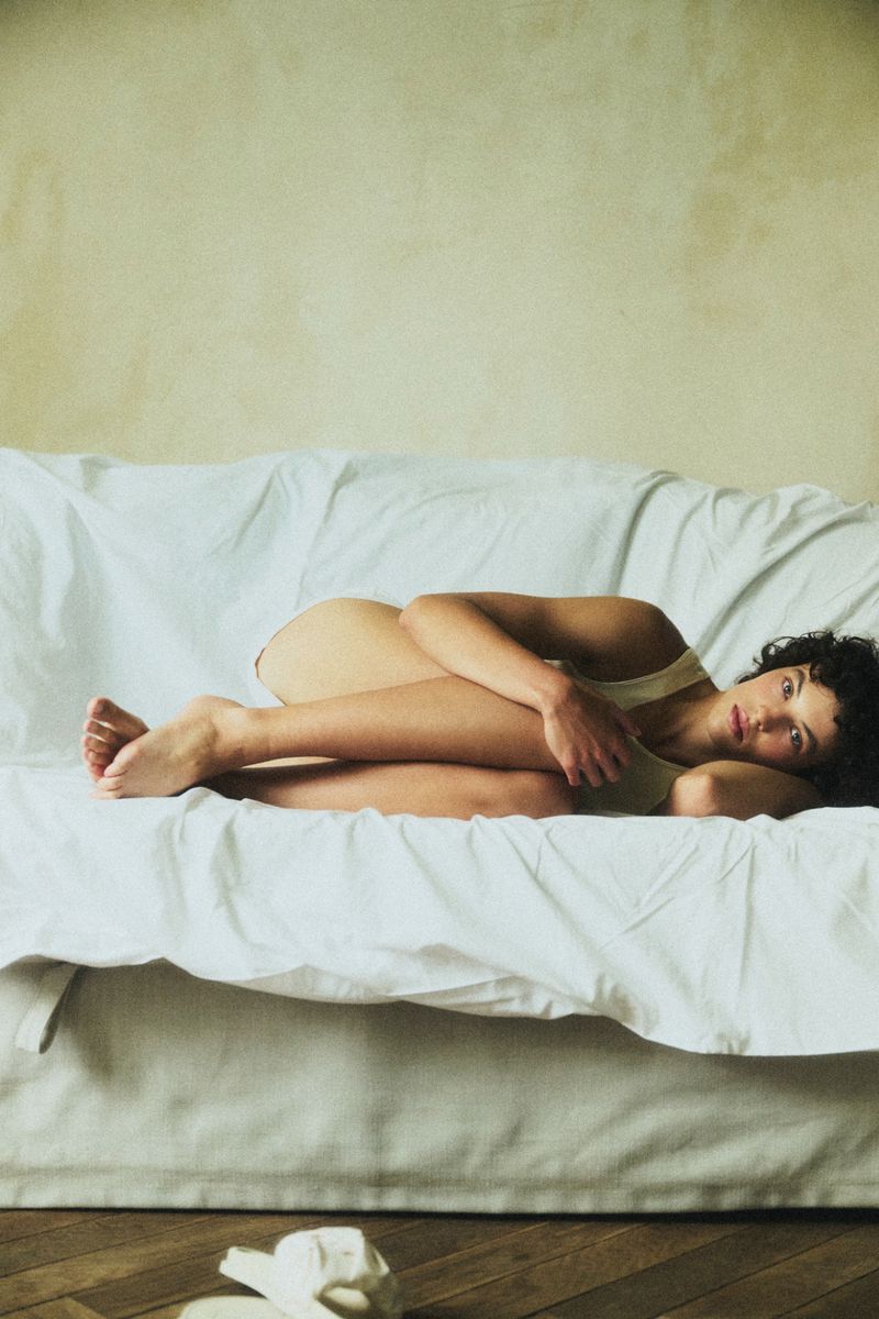 Model Maja Zimnoch curled up on a white fabric-covered sofa, photographed by Dorota Szulc for INUIKII x BOGDAO.