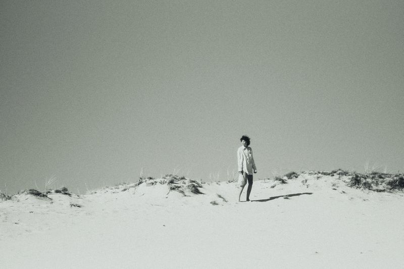 Model Maja Zimnoch stands atop a pale sandy dune against a vast sky in an outdoor fashion shoot by Dorota Szulc.