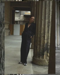 Model in a black patterned jumpsuit leaning against a large stone column in a covered walkway for Contributor Magazine.
