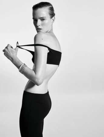 Model with slicked-back hair looking over shoulder while adjusting a black bandeau top against a white backdrop.