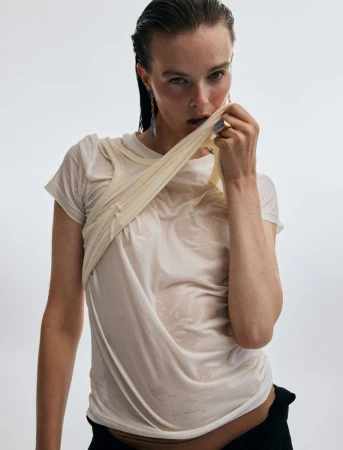 Model with wet slicked-back hair wearing a sheer wet cream t-shirt against a white background