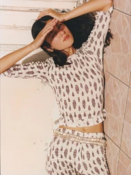 Mahalia Henderson lying down shading her eyes wearing a printed cream two-piece set against a pale tiled wall.