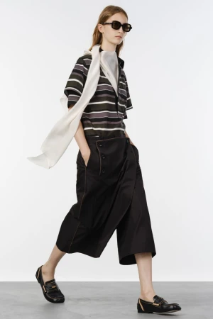 Model wearing a striped polo shirt, flowing white scarf, wide-leg black culottes, and loafers against a white backdrop.