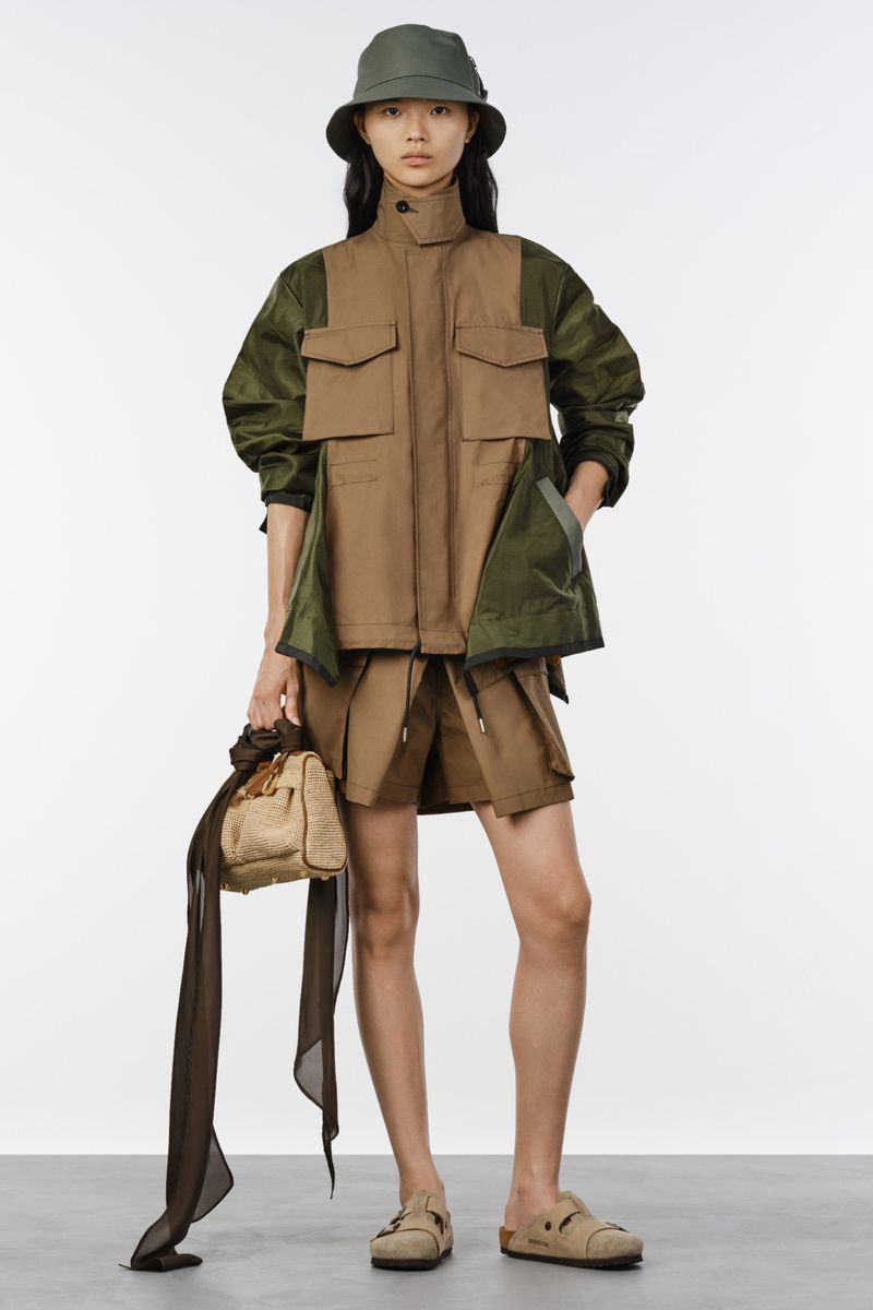 Model wearing a brown utility vest jacket, matching shorts, bucket hat, and sandals against a white studio background.