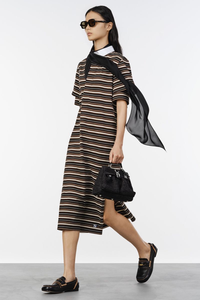 Model in a striped midi polo dress with sunglasses, a flowing black scarf, and loafers against a white studio background