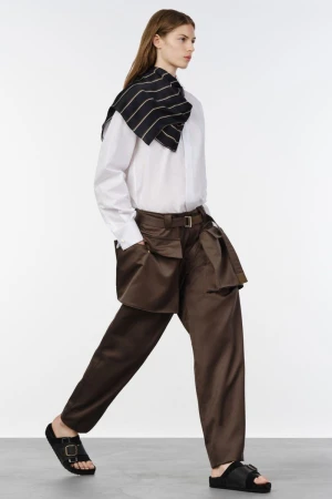 Model wearing a white button-down shirt and brown utility trousers walking across a bright white studio backdrop.