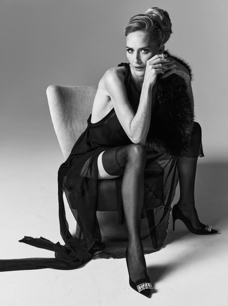 Monochrome portrait of a mature woman in an elegant dress, seated on a chair with fur stole, accessorized with high heels, in photo studio.