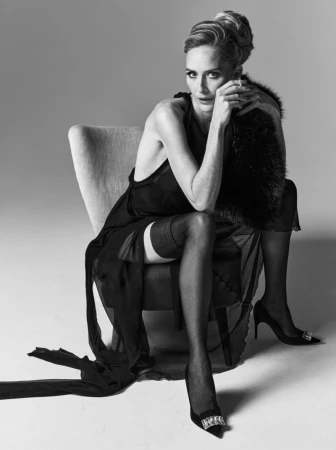 Monochrome portrait of a mature woman in an elegant dress, seated on a chair with fur stole, accessorized with high heels, in photo studio.
