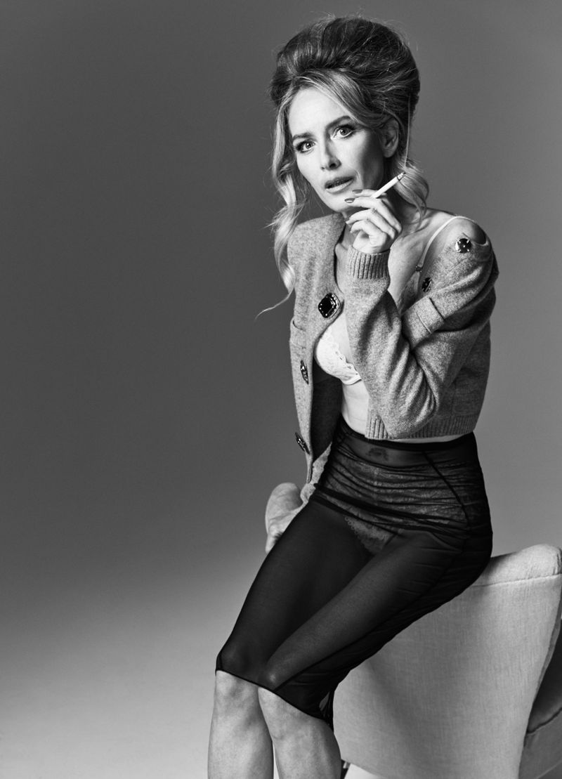 Black and white portrait of an adult female with an updo hairstyle smoking a cigarette while sitting on an armchair in a studio.