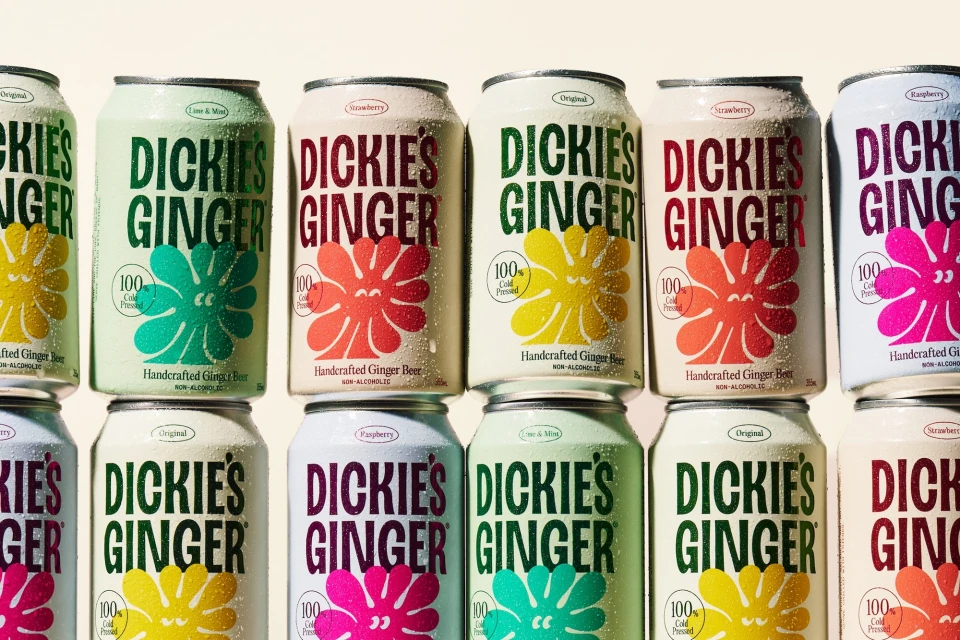 Rows of condensation-covered ginger beer cans featuring colorful graphic labels stacked closely together.