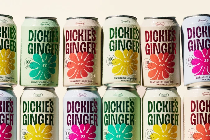 Rows of condensation-covered ginger beer cans featuring colorful graphic labels stacked closely together.