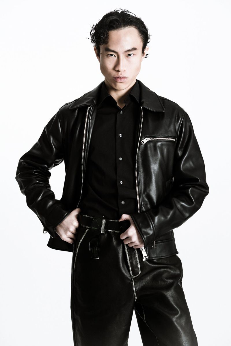 East Asian man in an all-black leather jacket, black shirt, and matching trousers posing against a bright white background.