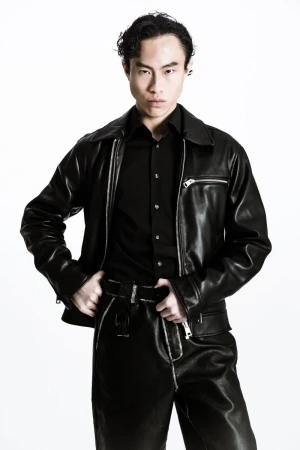 East Asian man in an all-black leather jacket, black shirt, and matching trousers posing against a bright white background.