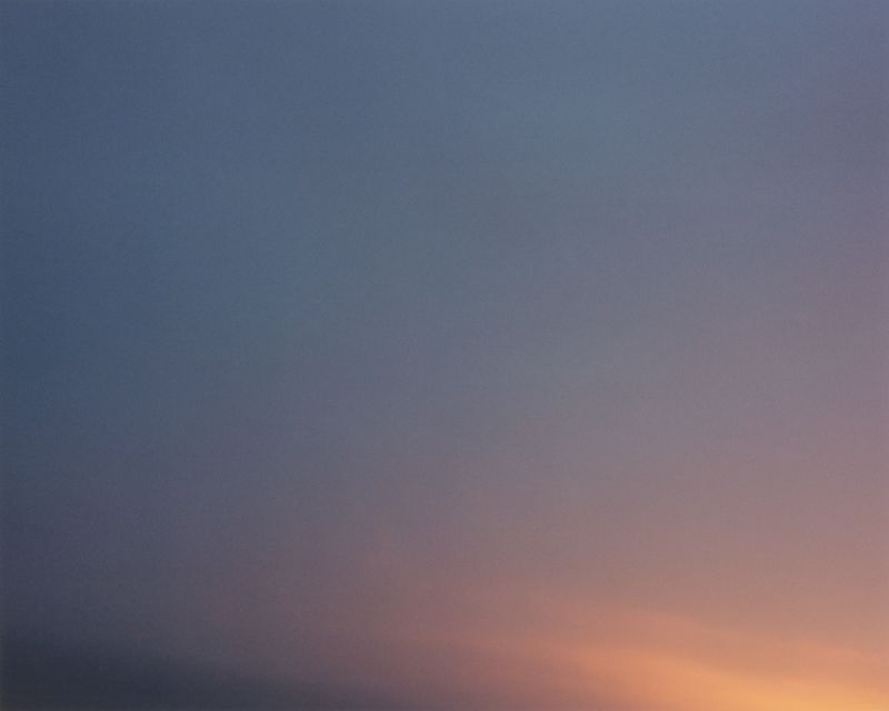 A soft gradient of deep twilight blue fading into a warm golden orange glow across an open evening sky.