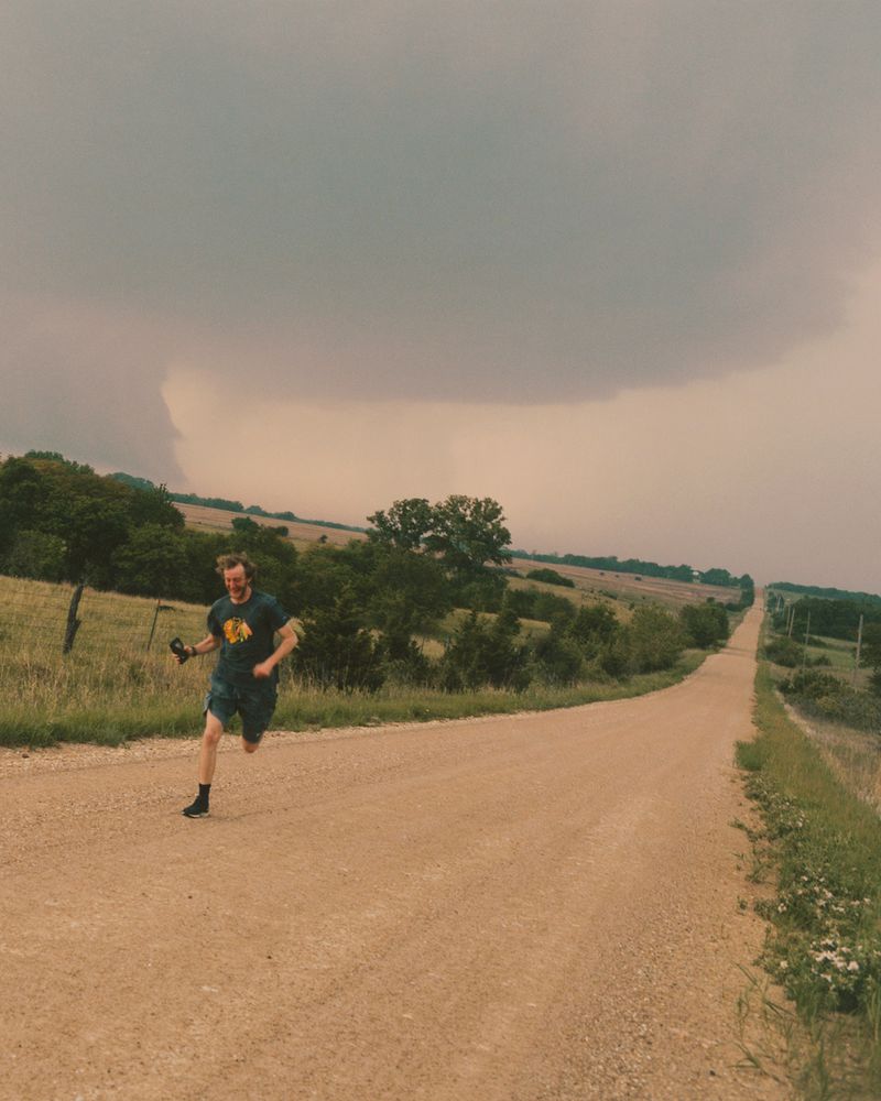 A man running along a dusty dirt road under a dark stormy sky for Atmos Magazine.
