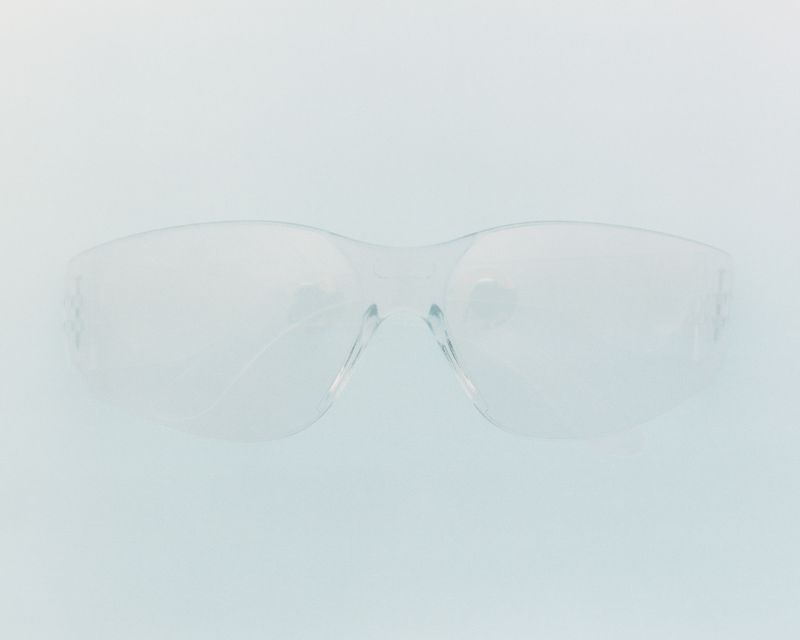 Clear transparent safety glasses centered against a minimalist pale blue-grey background.