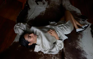 Woman wearing a pale silk blouse and shorts lying on a brown and white cowhide rug on a wood floor.