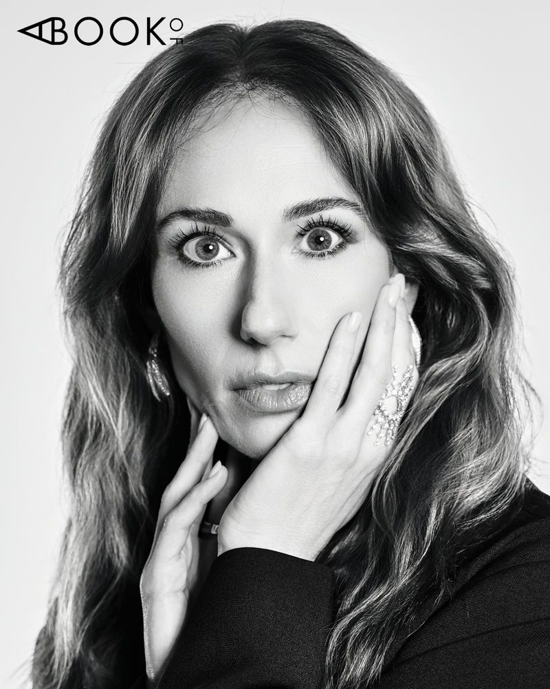 Black and white portrait of Jessica Blair Herman looking forward with hands on her cheek against a studio backdrop.