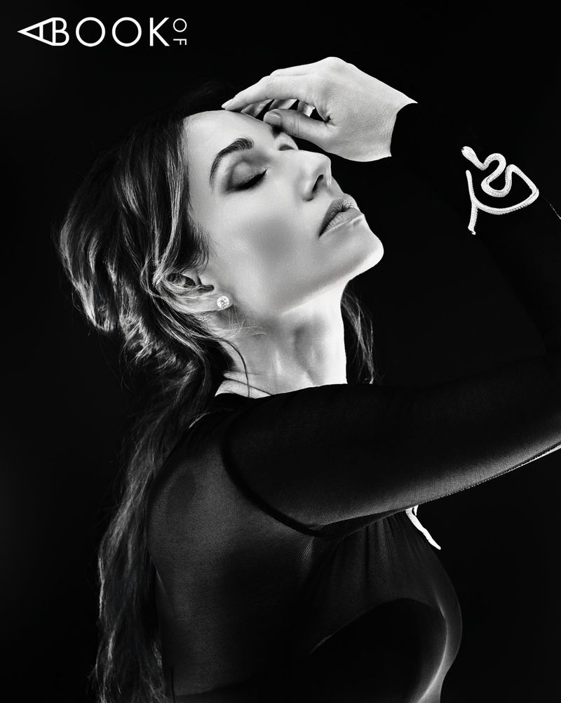 Black and white portrait of Jessica Blair Herman posing in profile with her hand to her head against a dark studio background.