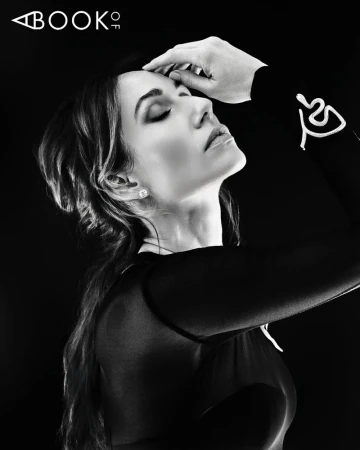 Black and white portrait of Jessica Blair Herman posing in profile with her hand to her head against a dark studio background.