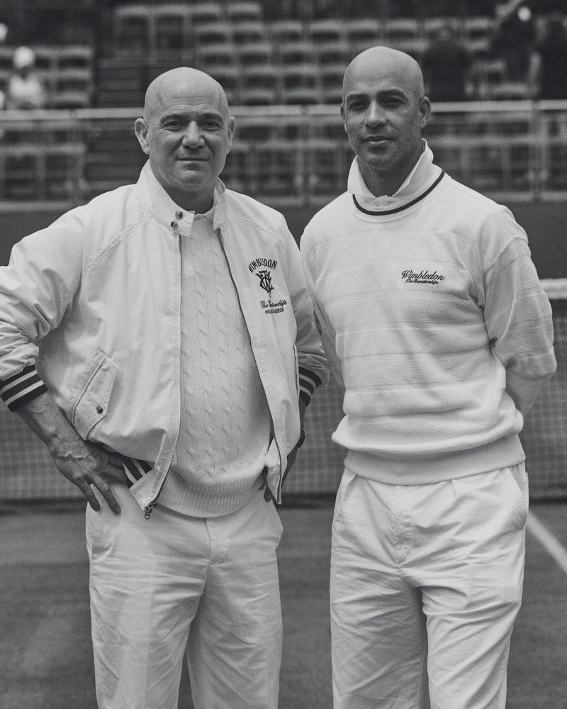 Two bald men standing on a tennis court wearing white Ralph Lauren Wimbledon sweaters and trousers in a black and white photograph