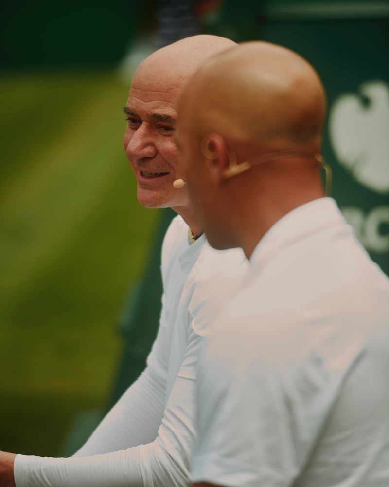 Andre Agassi wearing a white shirt and headset microphone conversing on the court at Wimbledon.