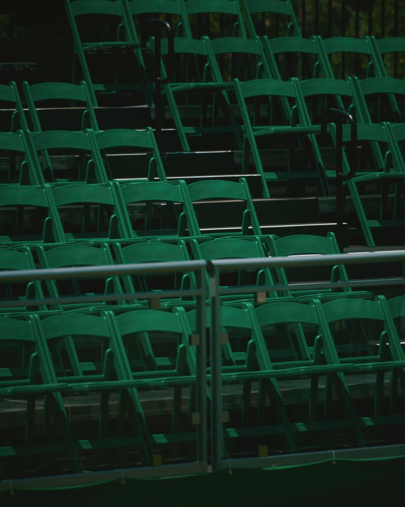 Empty dark green folding chairs arranged in rows on tiered grandstand bleachers behind a metal railing.