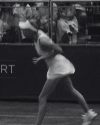 Black and white photograph of a tennis player in motion wearing a white visor and dress with spectators in the background.