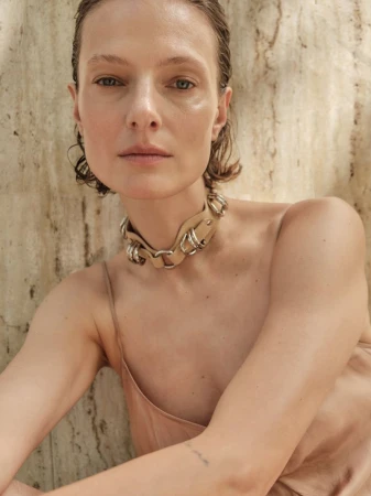 Close-up portrait of model Tanya Ruban wearing a beige leather choker and slip top against a textured stone wall.