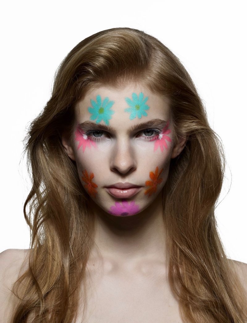Close-up beauty portrait of a woman with painted pastel floral makeup on her face against a plain white studio background.