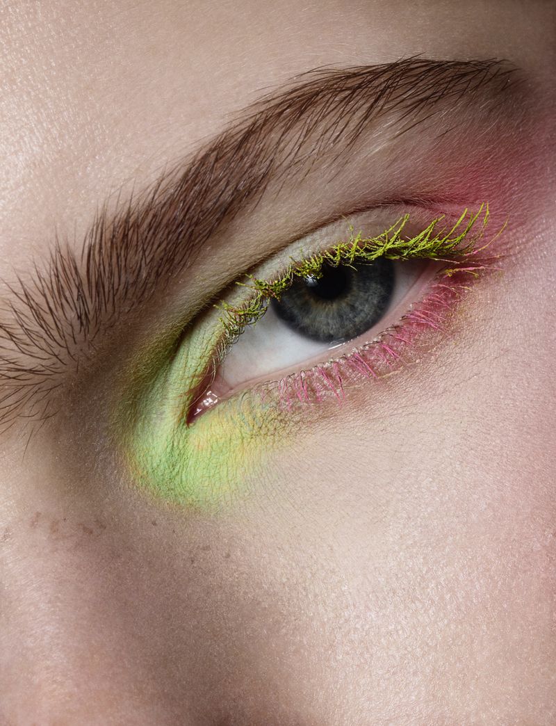 Macro close-up of a blue eye styled with textured lime green mascara and soft pink eyeshadow.