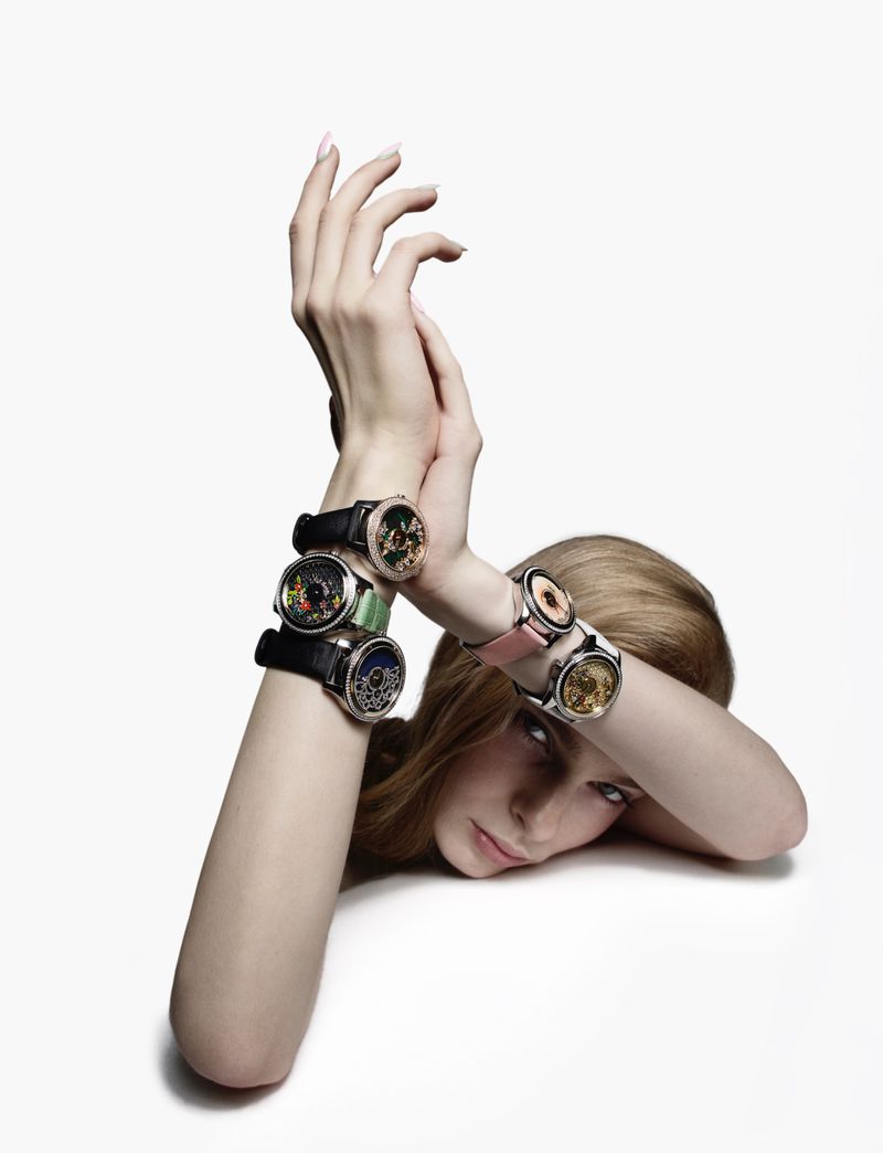 Model Victoria Volt resting her chin on a white surface with hands raised, wearing multiple luxury wristwatches on her arms.