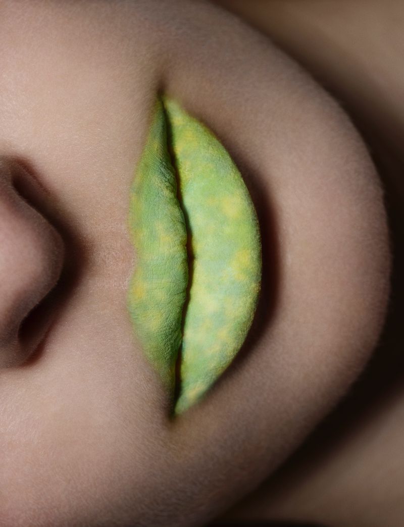 Extreme macro close-up of lips painted in a textured lime green and yellow shade, with visible skin texture.