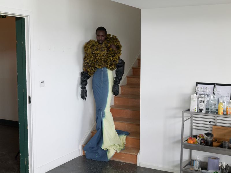 Elegant adult posing indoors on stairs in a statement ruffled top, long skirt, and gloves in a fashion editorial photo shoot.