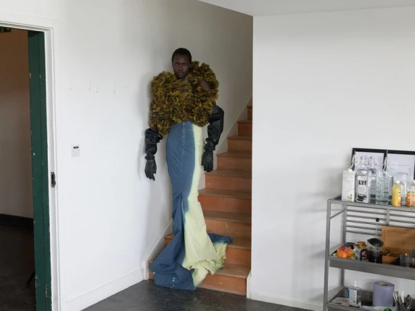 Elegant adult posing indoors on stairs in a statement ruffled top, long skirt, and gloves in a fashion editorial photo shoot.