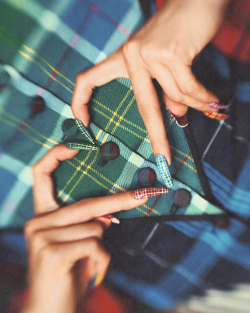 Close up of hands with plaid patterned manicured nails interacting with a green and blue plaid jacket