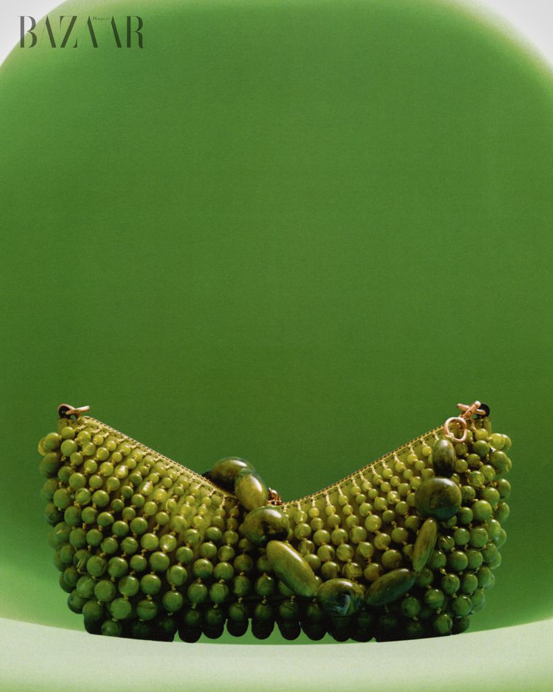 Green beaded handbag with polished statement beads resting on a curved lime green surface for Harper's Bazaar Vietnam.